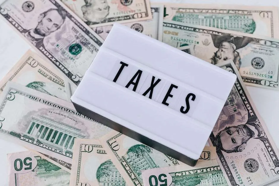 A white lightbox displaying the word "TAXES" in black capital letters, placed on top of a background of U.S. dollar bills.